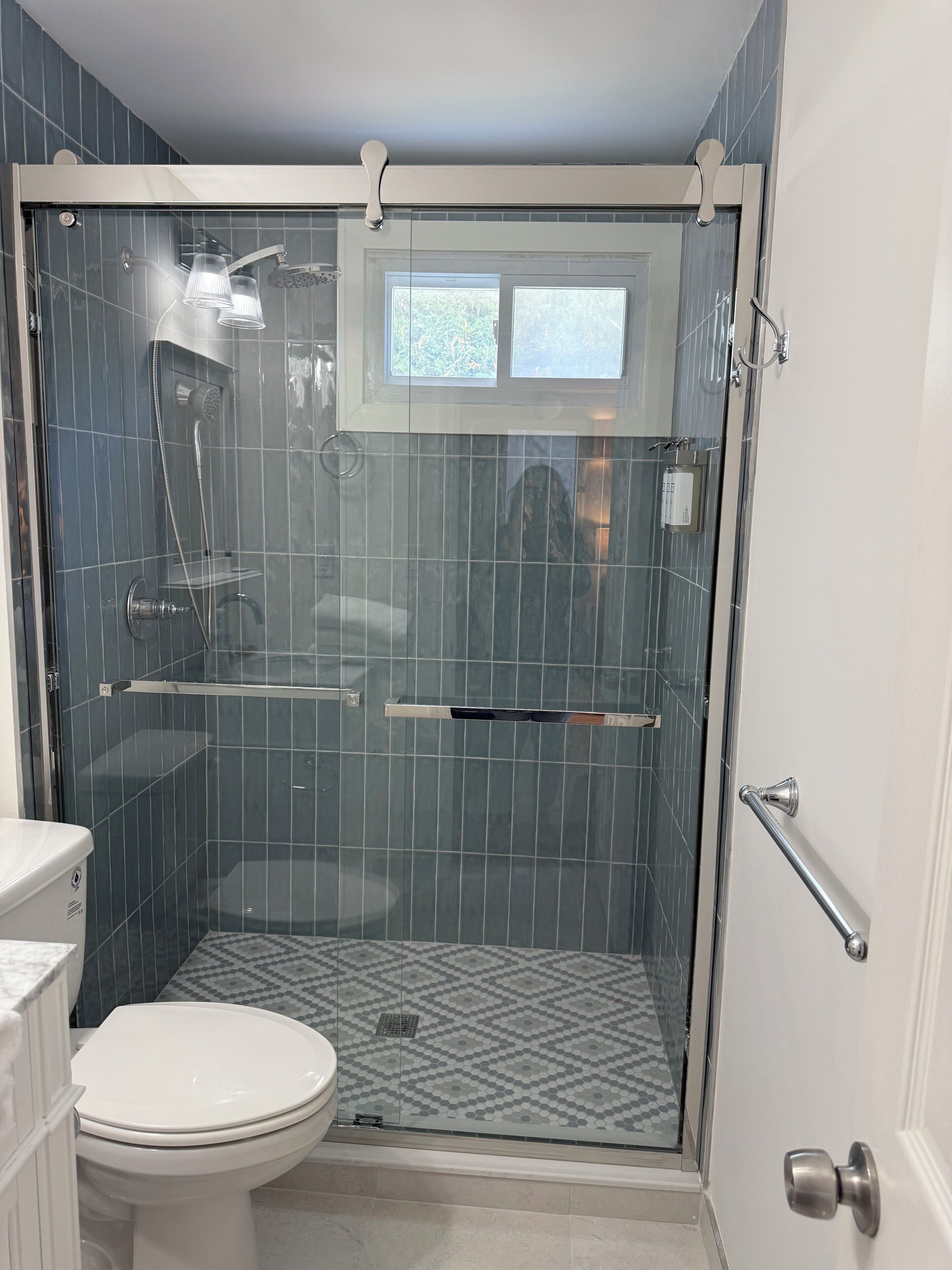 A bathroom with a glass-enclosed shower, a toilet, and a window above the shower.