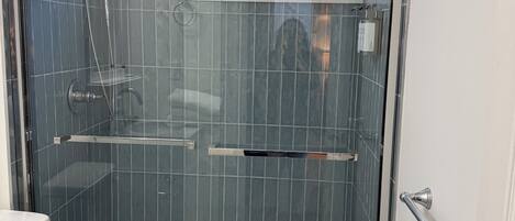 A bathroom with a glass-enclosed shower, a toilet, and a window above the shower.