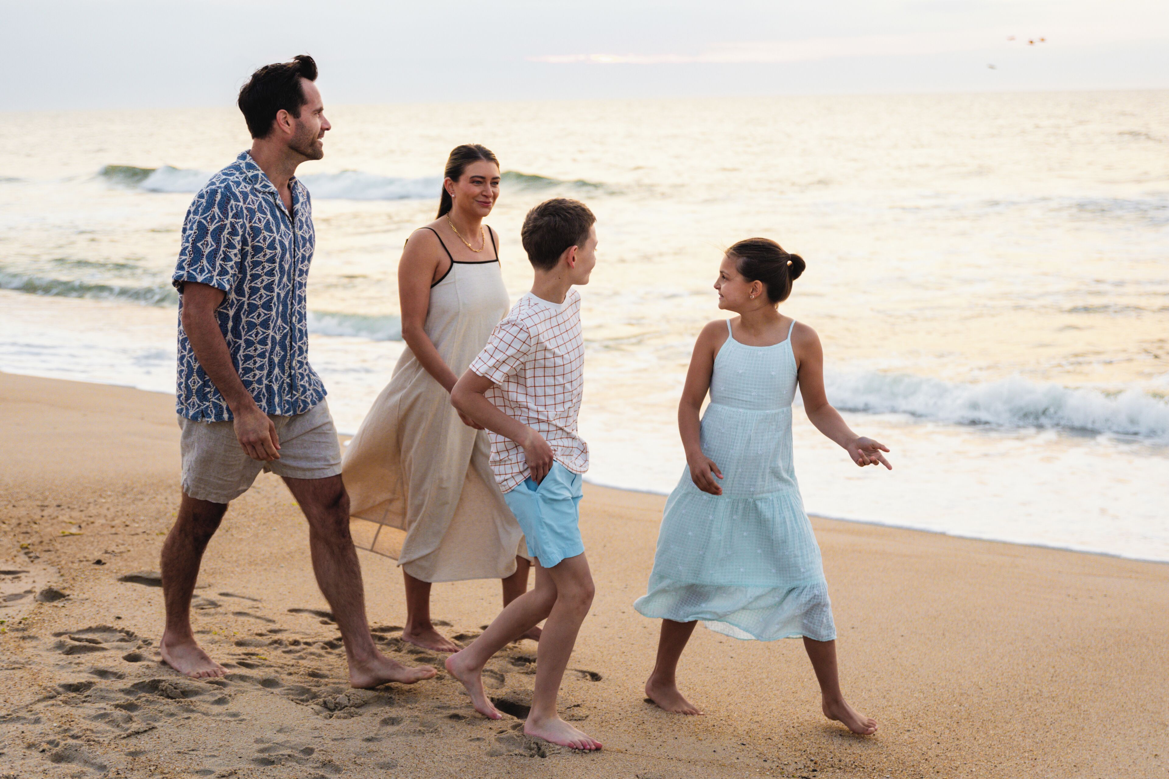 Eine Familie spaziert am sandigen Strand, im Hintergrund das Meer.