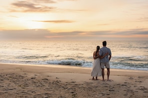 A couple standing on a beach with the ocean and a sunset in the background. - Oceana By The Sea (Point Pleasant Beach)