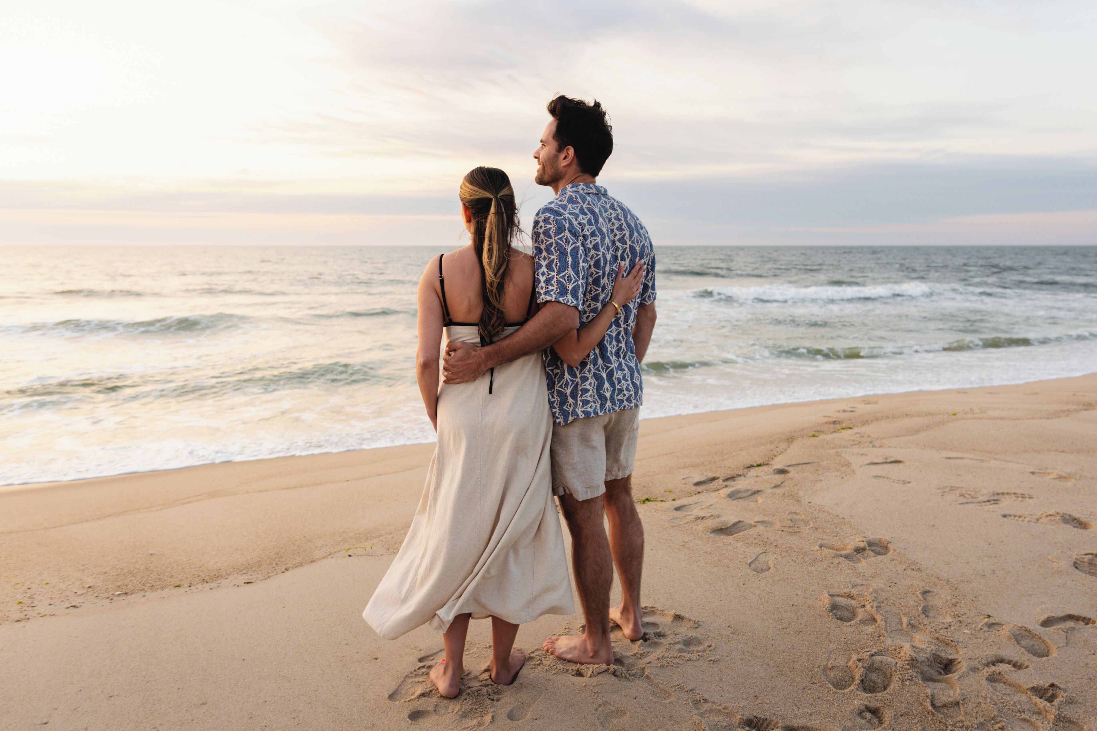 A couple standing on a sandy beach with ocean waves in the background.