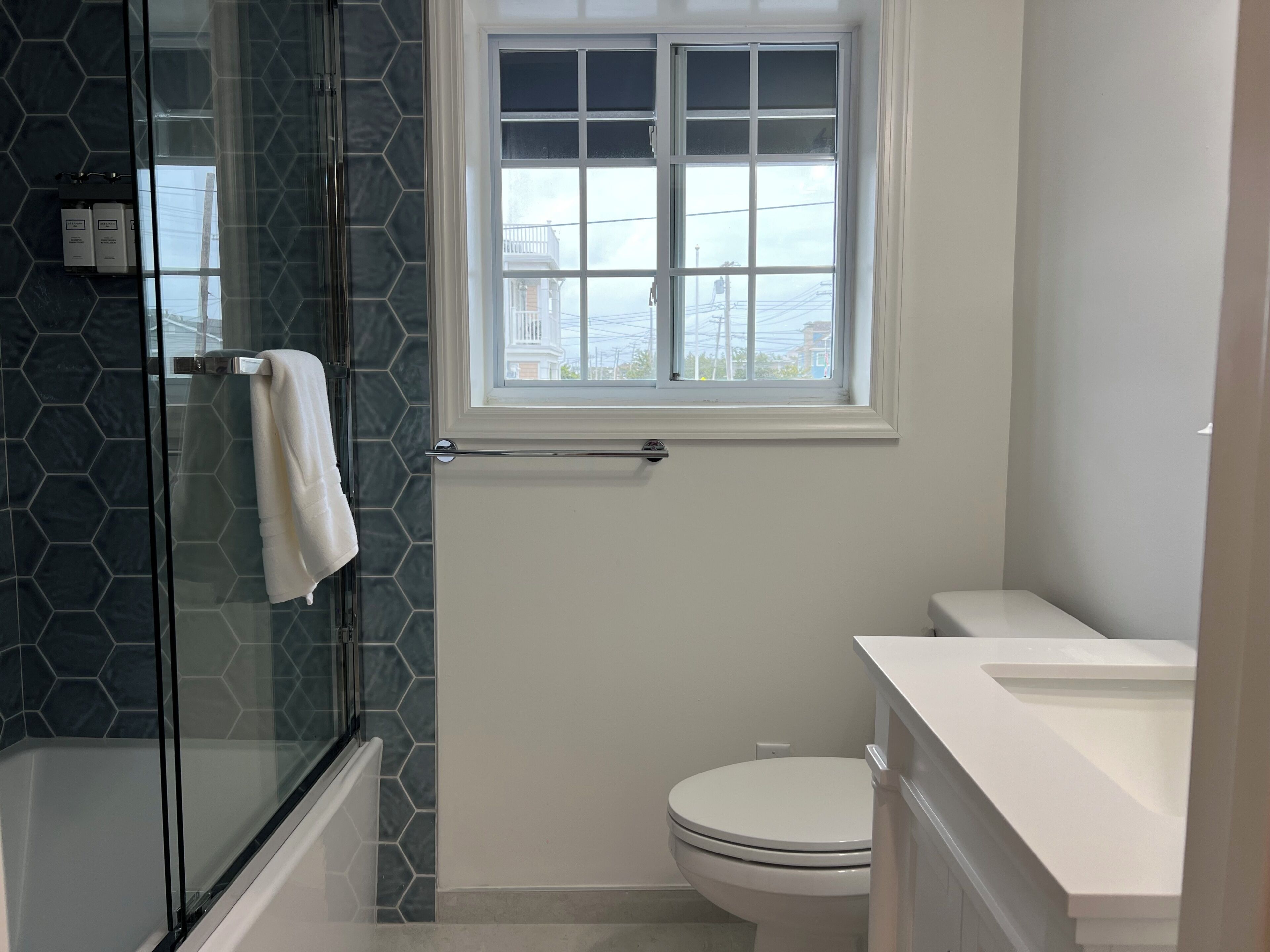 A bathroom with a glass shower enclosure, a white toilet, and a window with a view of the outside.