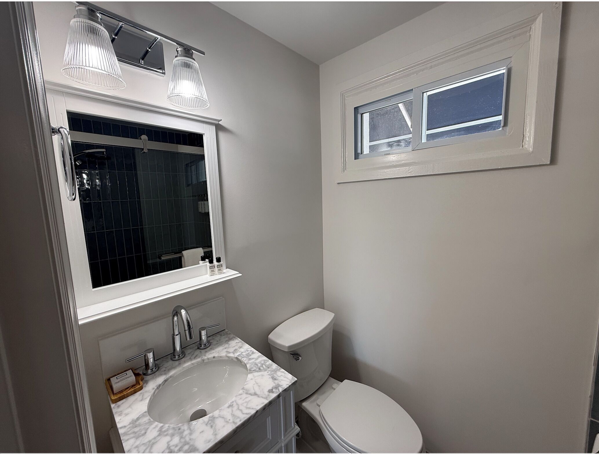A bathroom with a white sink, a mirror, a toilet, and a window.