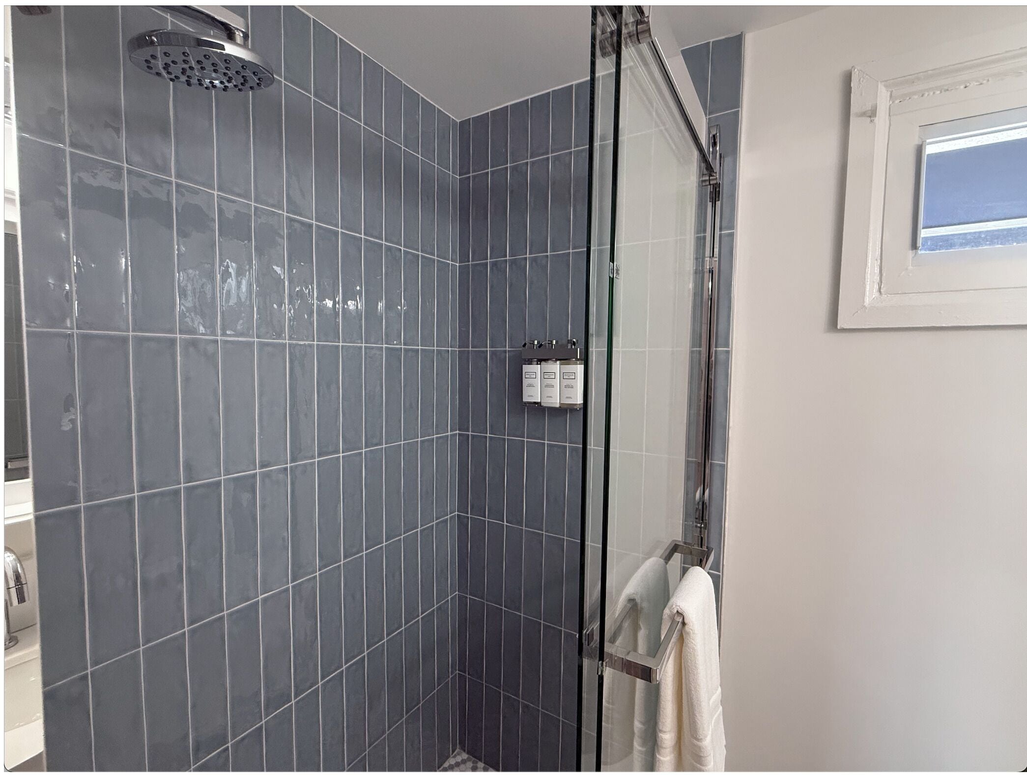 A shower with a glass door, a white towel hanging on a rack, and a window with a view.