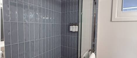 A shower with a glass door, a white towel hanging on a rack, and a window with a view.