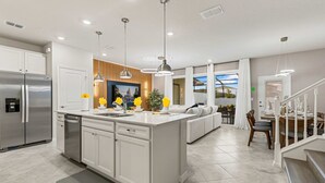 Une cuisine moderne dotée d’un îlot central, d’appareils électroménagers en acier inoxydable et de luminaires suspendus.