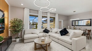 Un salon moderne avec un canapé d’angle, une table basse ronde et une grande fenêtre avec des rideaux.