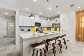 A modern kitchen with white cabinets, stainless steel appliances, and a central island with bar stools. - Brand New | 5BR Pool Home w Safari Loft 16200 (Clermont)