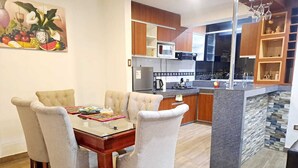 Una cocina moderna con una isla central, armarios de madera y un comedor con mesa de vidrio y sillas acolchadas.