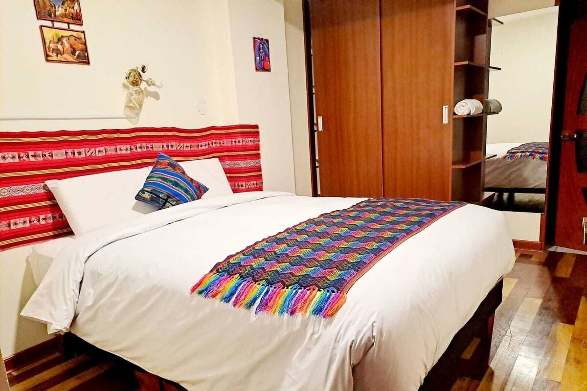 A bed with a colorful blanket, a wooden headboard, and a red-striped pillow.
