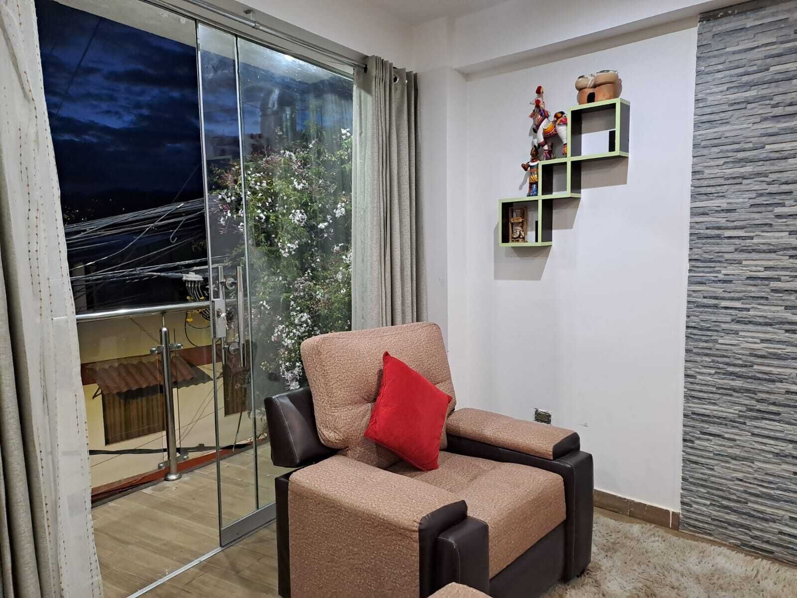 A modern living room with a sofa, a red cushion, a glass door leading to a balcony, and a stone-textured wall.