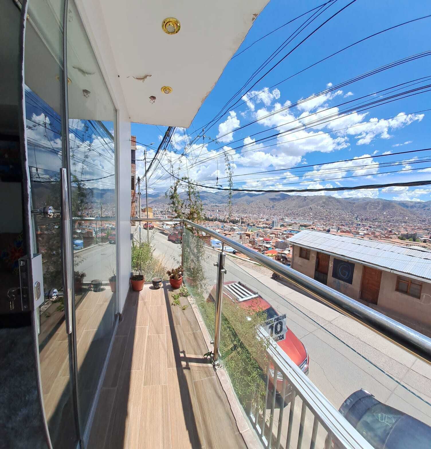 A balcony with a city view, power lines, and a red car on the street.
