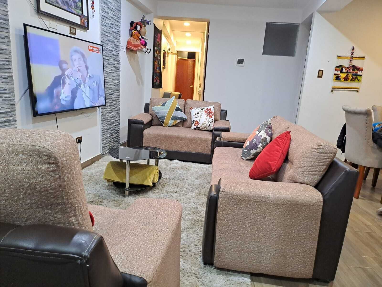 Una sala de estar con sofá, sillones, una mesa de centro y televisor.