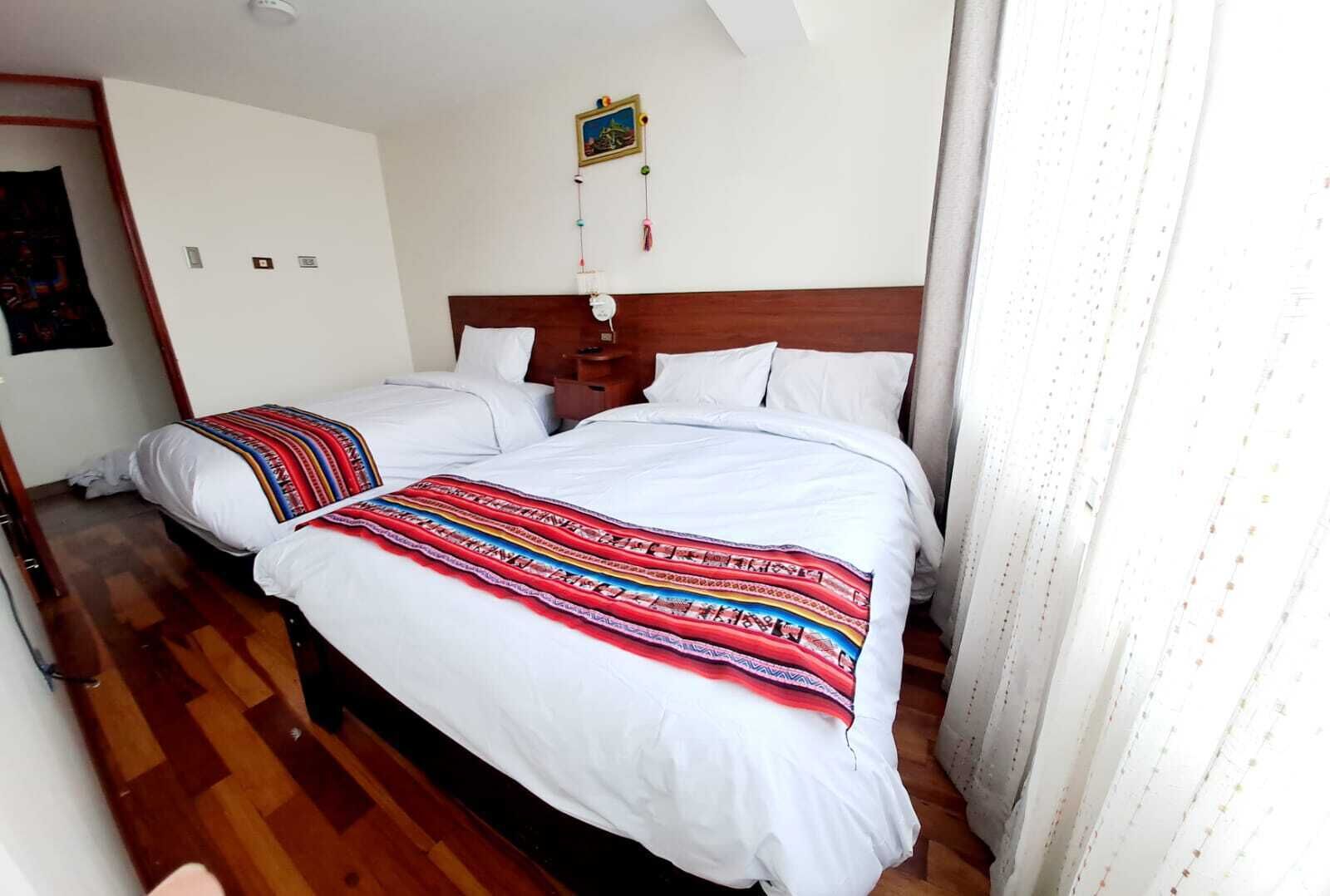Een hotelkamer met twee bedden, een houten vloer, een witte muur en een klein schilderij boven de bedden.