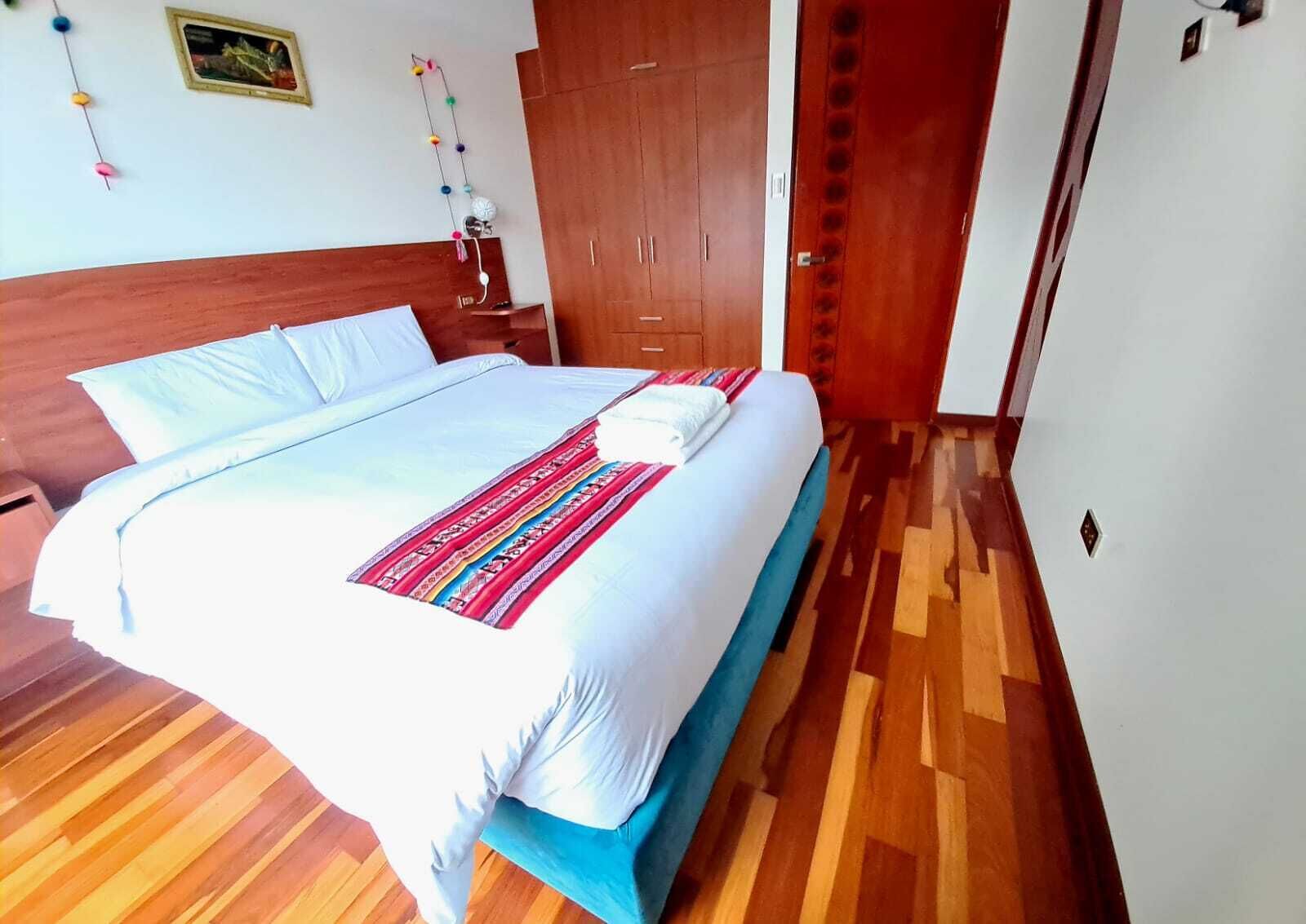 A neatly made bed with a patterned blanket, wooden flooring, a wooden wardrobe, and a door with circular cutouts.