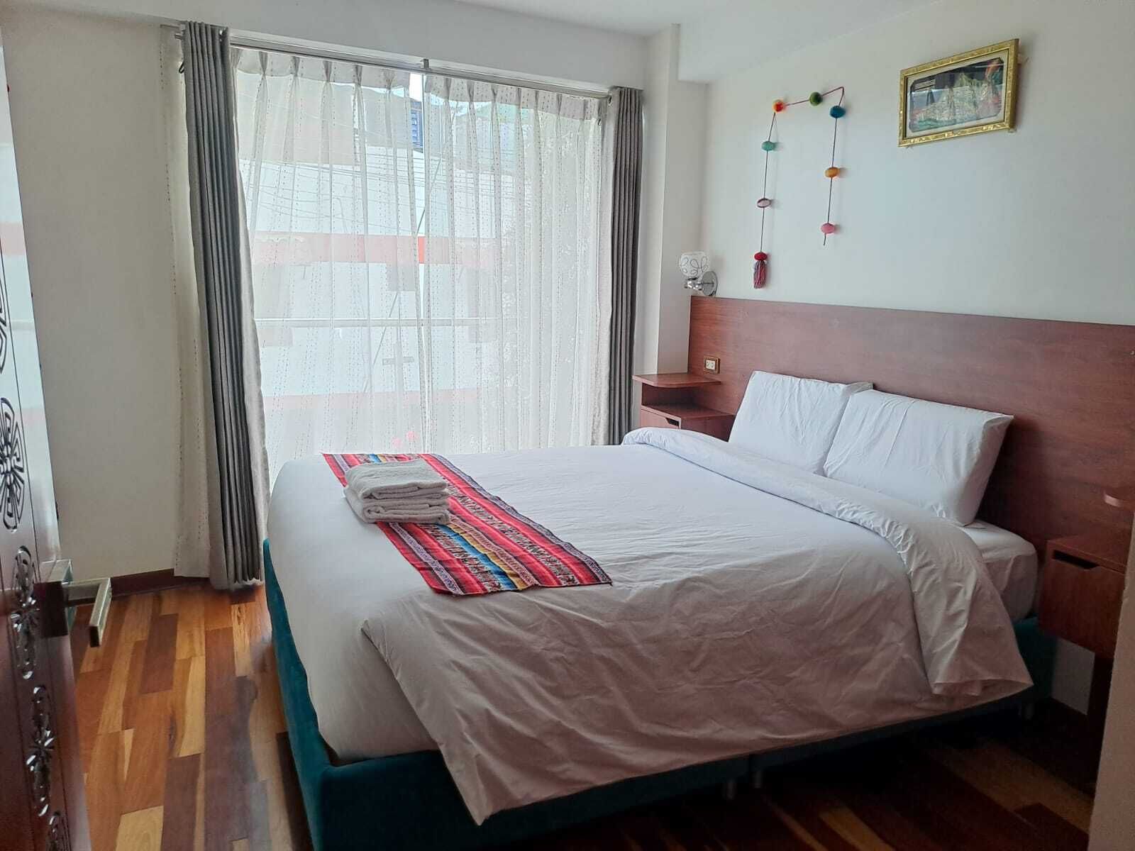 Ein Hotelzimmer mit einem Bett, einem Nachttisch, einem Fenster mit Vorhängen und einem Wandbild.