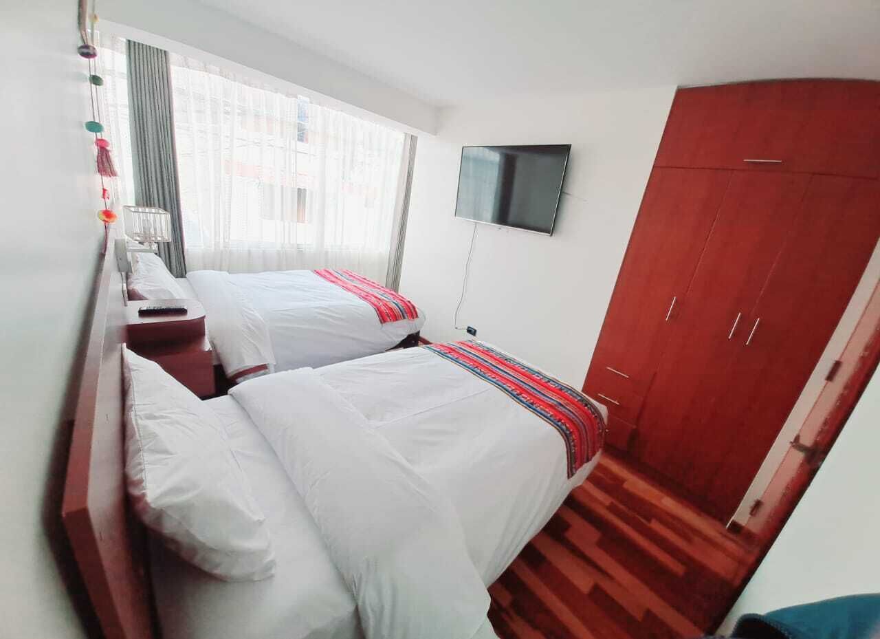 Habitación de hotel con dos camas, televisión, armario y ventana con cortinas.