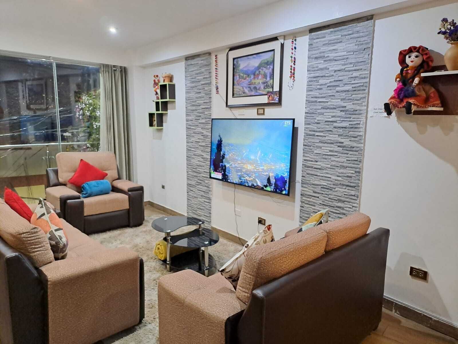 Un salon moderne doté d’un grand téléviseur à écran plat fixé sur un mur à texture, d’un ensemble de canapés, d’une table basse et d’une petite table d’appoint.