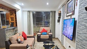 Una sala de estar con un conjunto de sofá, una mesa de centro, un televisor y una pared con textura de piedra.