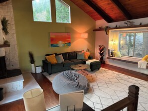 Ein gemütliches Wohnzimmer mit Kamin, einer Couch, einem Couchtisch und einem Fenster mit Blick auf Bäume.