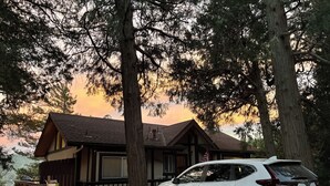 Un SUV blanco estacionado frente a una cabaña con terraza de madera y un árbol grande.