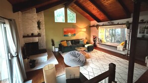 Una sala de estar acogedora con chimenea de piedra, un sofá, una mesita de centro y un ventanal con vistas a árboles.