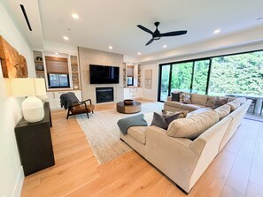 A modern living room with a fireplace, sofa, TV, and large windows. - Spacious 5-bedroom house in beautiful Manhattan Beach with AC and great yards (Manhattan Beach)