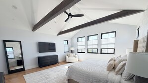 Ein Schlafzimmer mit einem großen Bett, einem Deckenventilator, einem Fernseher und einem Fenster mit Jalousien.