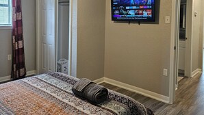 A bedroom with a bed, a ceiling fan, a television on the wall, and a door leading to another room. - Adorable 3-bedroom 2 bath house with AC calm in wooded area near the Woodlands (Conroe)