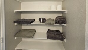 A closet with multiple shelves, some holding folded towels and mittens. - Adorable 3-bedroom 2 bath house with AC calm in wooded area near the Woodlands (Conroe)