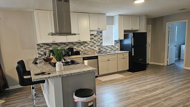 A modern kitchen with white cabinets, a granite countertop, a stainless steel range hood, and a black refrigerator. - Adorable 3-bedroom 2 bath house with AC calm in wooded area near the Woodlands (Conroe)