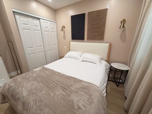 Une chambre à coucher comprenant un lit, une petite table ronde, une armoire et deux lampes fixées au mur.