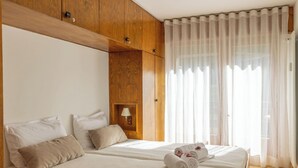 Een hotelkamer met twee bedden, houten lambrisering, een nachtkastje met een lamp en dunne gordijnen.
