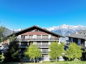 Ein mehrstöckiges Gebäude mit Balkonen, einem Berg im Hintergrund und blauem Himmel.