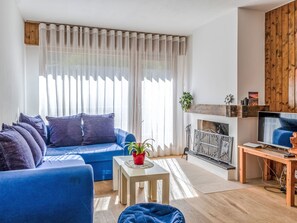 Ein Wohnzimmer mit einem blauen Sofa, einem kleinen Tisch mit Pflanze, einem Kamin und einem Fernseher.