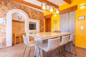 Une cuisine dotée d’un grand îlot central, de chaises blanches, d’un mur en pierre et d’un plafond en bois.