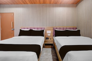 A hotel room with two beds, a wooden headboard, a small wooden nightstand, and a door.