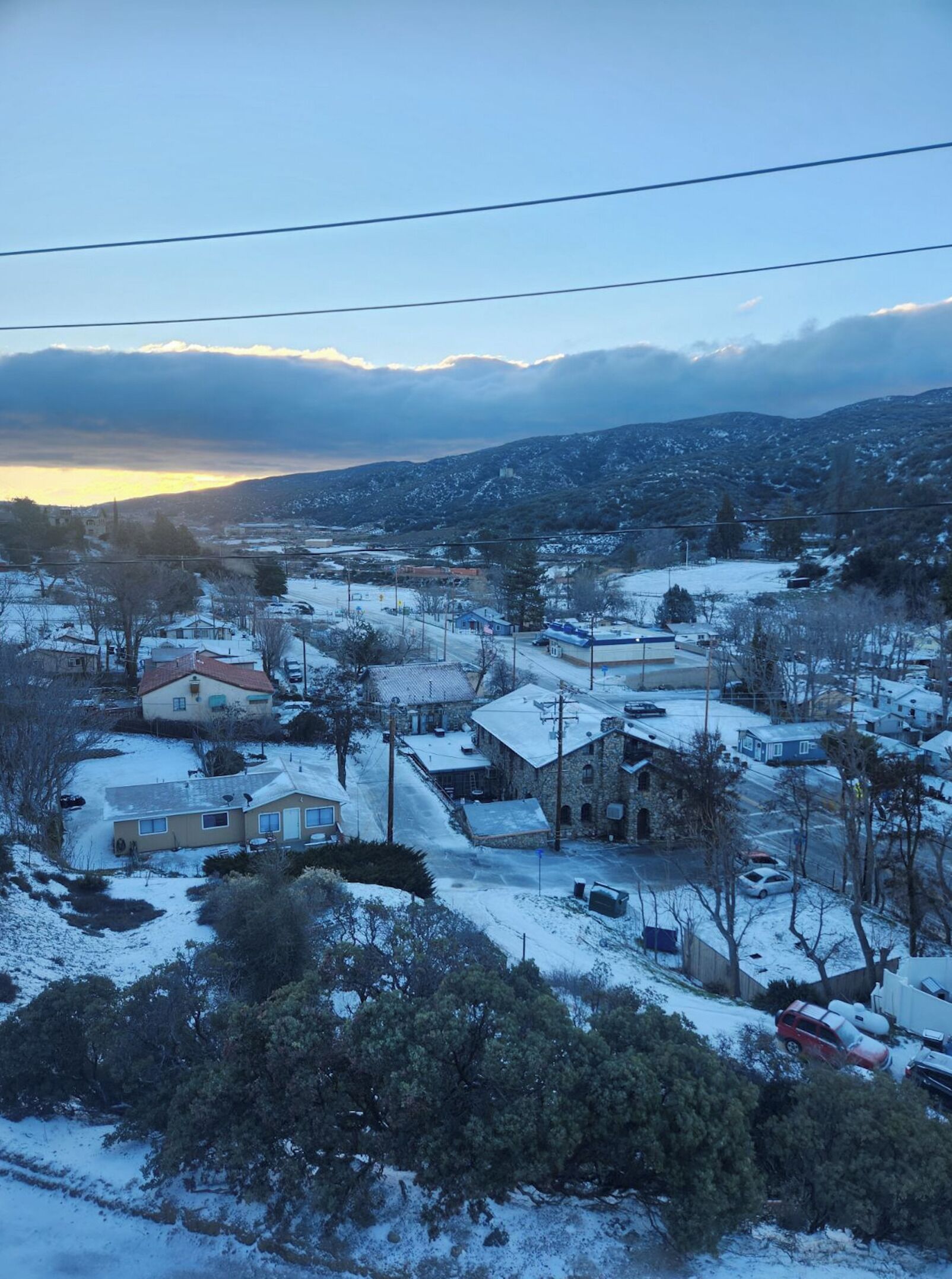 A snow-covered residential area with houses, a stone building, and a distant mountain range.