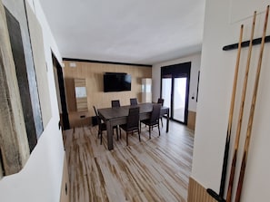 A modern dining area with a wooden table and chairs, a mounted TV, and a view through a glass door. - VILLA CALA LLARGA BEACH (Roses)