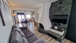 A modern living room with a grey sectional sofa, a stone fireplace, and a flat-screen TV mounted on a marble wall.