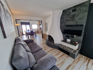 Una sala moderna con un sofá seccional gris, una chimenea de piedra y un televisor de pantalla plana montado en una pared de mármol.
