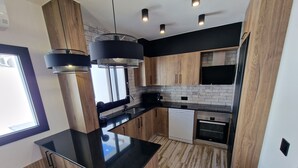 A modern kitchen with wooden cabinets, a black countertop, and pendant lighting.