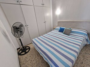 Une chambre à coucher avec un lit, un ventilateur et une armoire.