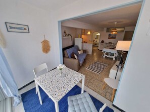 A modern living room with a sofa, a dining table, and a kitchen area visible through an open doorway. - KARINA APARTMENT BEACH-6 (Empuriabrava)