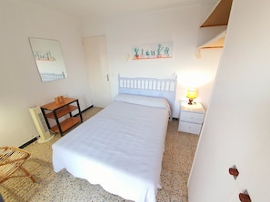 Ein Schlafzimmer mit Bett, Nachttisch, Lampe, Sessel und Wandregal.