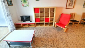 Een kamer met een bed, een televisie, een rode stoel, een houten kast en kunstwerken aan de muur.