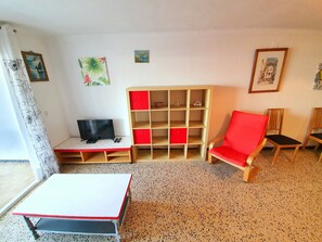 A room with a bed, a TV, a red chair, a wooden cabinet, and artwork on the walls. - KARINA APARTMENT BEACH-3 (Empuriabrava)