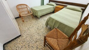 Een kamer met twee éénpersoonsbedden, een houten stoel, een klein houten tafeltje en een raam met een groene gordijn.