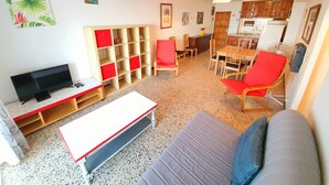 Een woonkamer met een televisie, rode en witte meubels, een eethoek en een keuken.