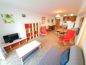A living room with a TV, red and white furniture, a dining area, and a kitchen. - KARINA APARTMENT BEACH-3 (Empuriabrava)